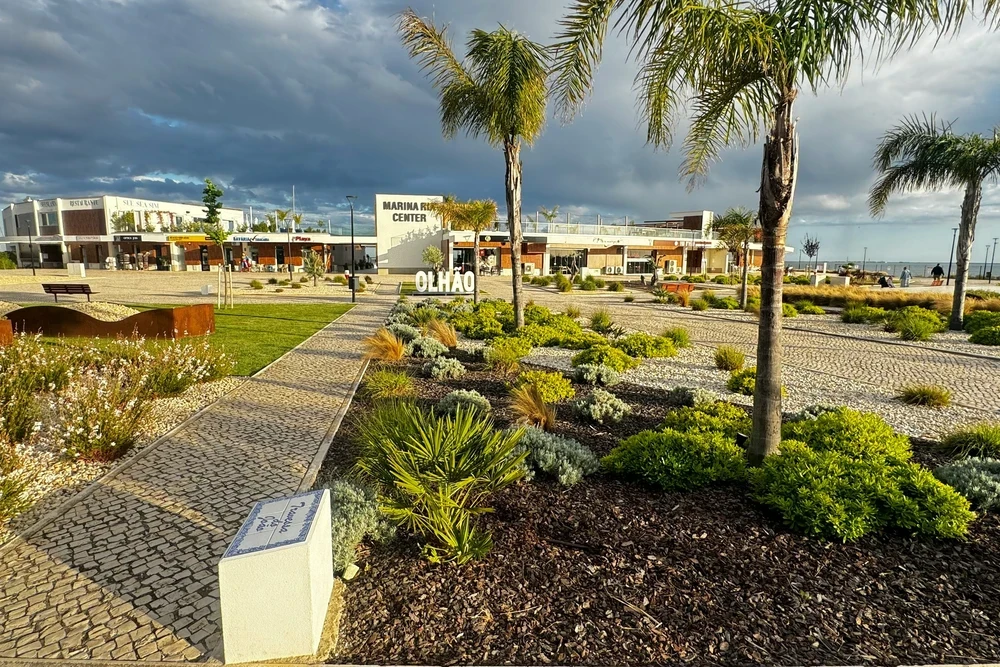 Modern Olhão Marina Center sign with lush palm trees and coastal landscaping under a dramatic cloudy sky in Olhao, Portugal.