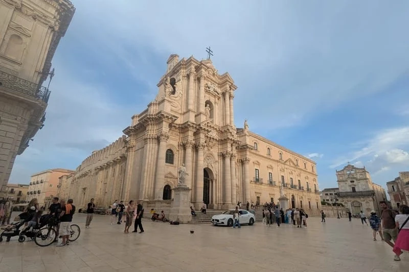 Piazza Duomo in Ortigia, Syracuse, Sicily, Italy, featuring the stunning baroque Cathedral of Syracuse with people walking in the square.