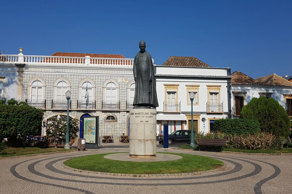 Statue of Dom Marcelino Franco in Praça Dr. António Padinha square, framed by traditional Portuguese buildings in Tavira.