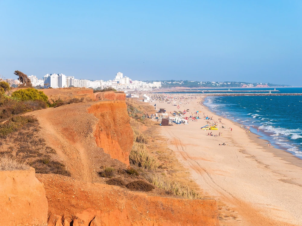 The iconic red cliffs overlooking the long stretch of golden sand and blue ocean at Praia da Falésia beach in Vilamoura.