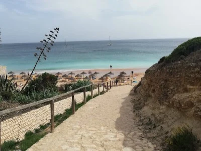 A charming cobblestone path winding down through vegetation to Praia da Mareta with calm turquoise waters in Sagres.