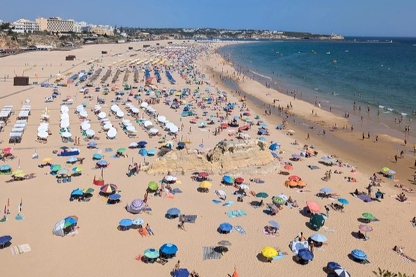 Aerial view of Praia da Rocha beach in Portimão, Algarve, Portugal, with colorful umbrellas, sunbathers, and golden sand stretching along the coast.