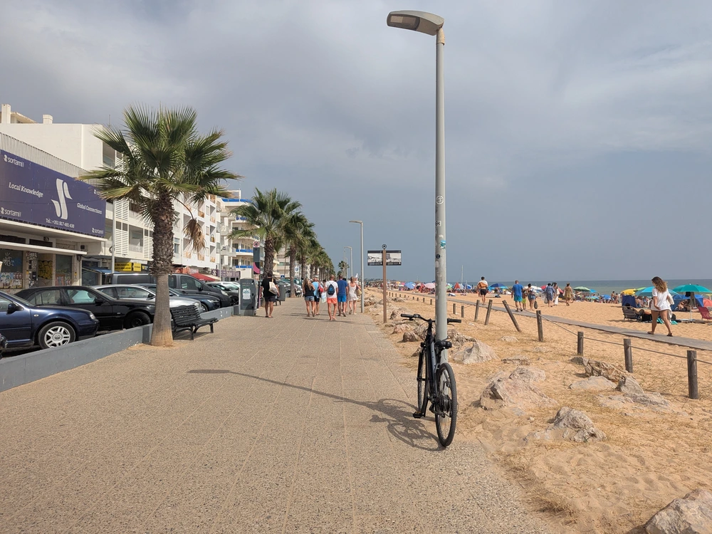 People strolling along the palm-lined beachfront promenade next to the sandy beach in Quarteira, Portugal.