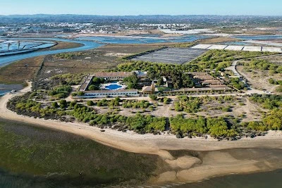 Aerial view of Praia dos Tesos and the adjacent Tavira salt pans, showing the lagoon, beach, and nearby building complex.
