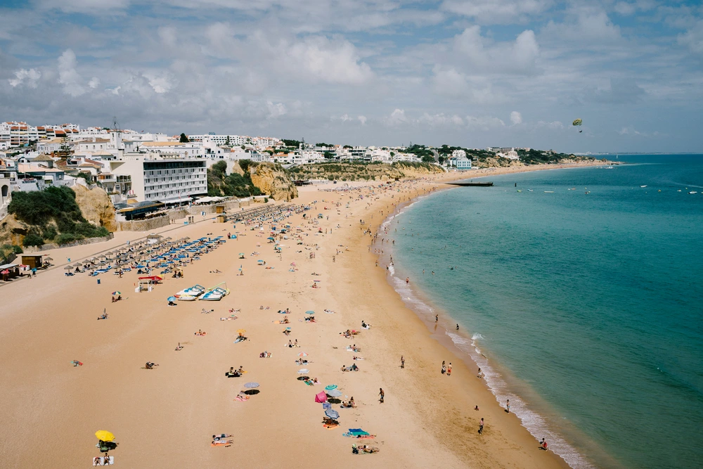 A beautiful aerial view of Praia do Peneco, one of the main beaches in Albufeira, bustling with sunbathers on the golden sand next to the calm turquoise sea.