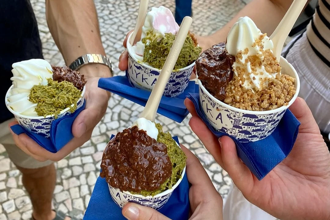 A group enjoying delicious cups of Myka frozen Greek yogurt on a cobblestone street in Lisbon.