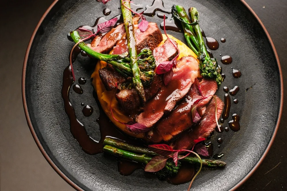 Gourmet dish with asparagus, sweet potato mash, and dark sauce, served on a black plate at Restaurante Bossa in Tavira, Portugal.