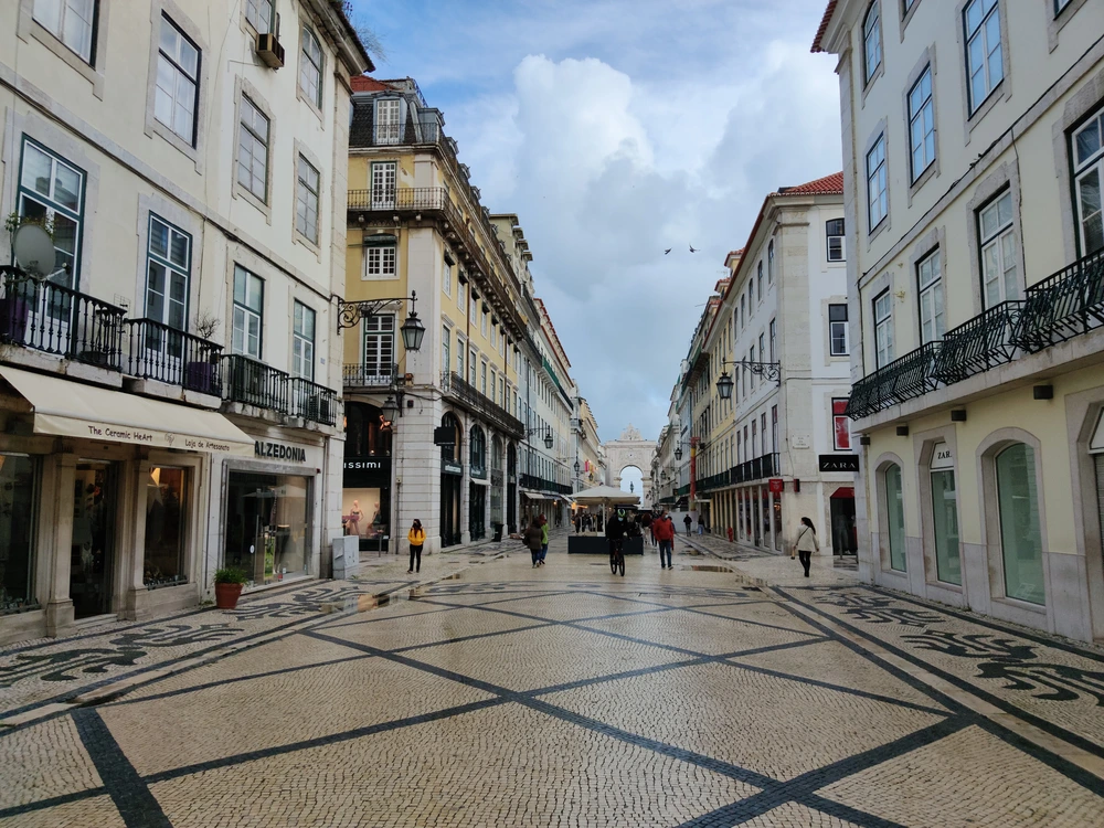 A wide, pedestrian cobblestone street with distinctive patterns, lined with classic European-style buildings on the Rua Augusta Shopping Street in Lisbon