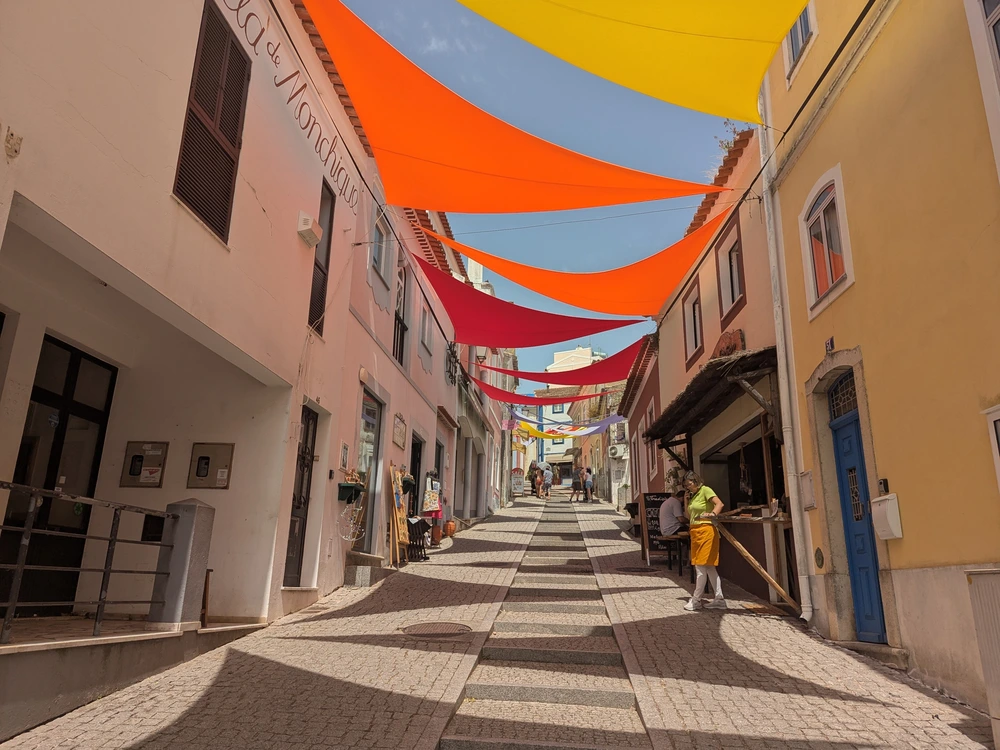 The charming Rua do Porto Fundo shopping street in Monchique, decorated with colorful fabric canopies shading the cobblestones below.