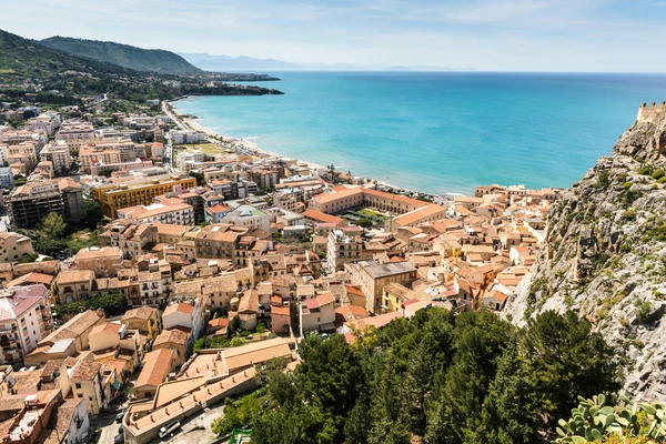 Scenic view of Cefalù, Sicily, Italy, featuring terracotta rooftops, historic buildings, and the turquoise Mediterranean Sea along the coastline.