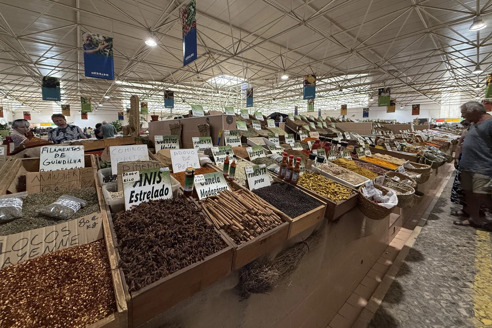 A wide array of spices, dried herbs, and regional products displayed in wooden crates at the bustling Mercado Municipal de Tavira.