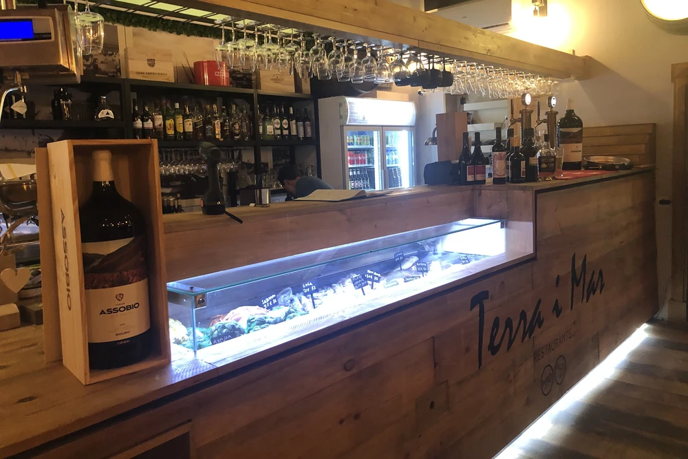 Interior view of Terra i Mar restaurant bar counter featuring fresh seafood display and a large bottle of wine in Olhao, Portugal.