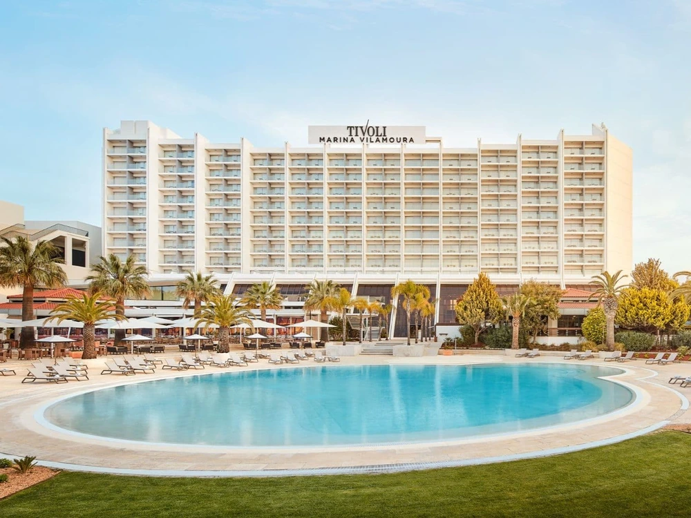 The impressive Tivoli Marina Vilamoura hotel with its large, circular swimming pool and sun loungers set against a clear blue sky.