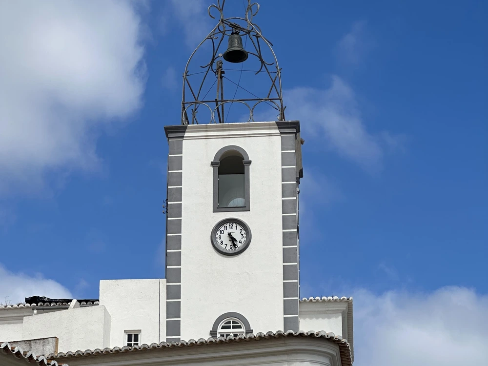 Close-up of the historic Torre de Relógio, the iconic white and grey clock tower in Old Town Albufeira, set against a bright blue sky.
