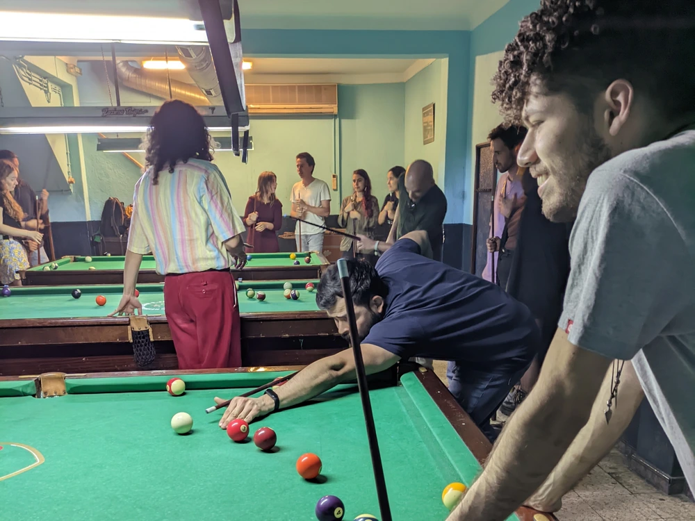 A lively scene inside the Tubarões da Atalaia pool bar in Lisbon's Bairro Alto, with a group of friends gathered around a green pool table.
