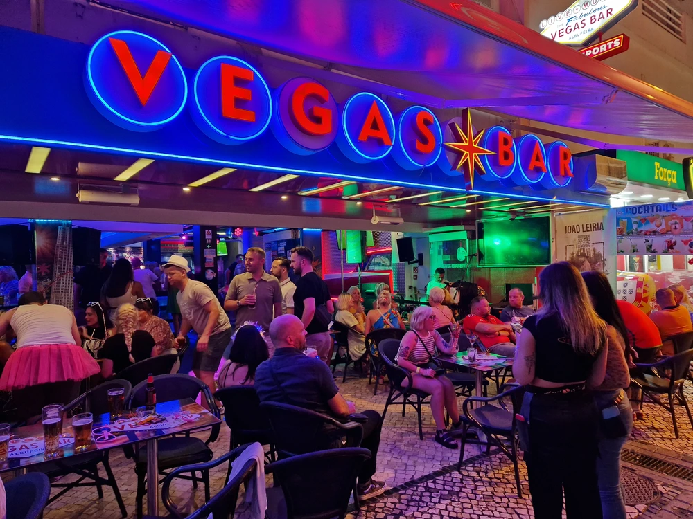 The vibrant atmosphere of Vegas Bar in Albufeira, a popular spot for live music, with its glowing neon sign and a crowd enjoying the nightlife.