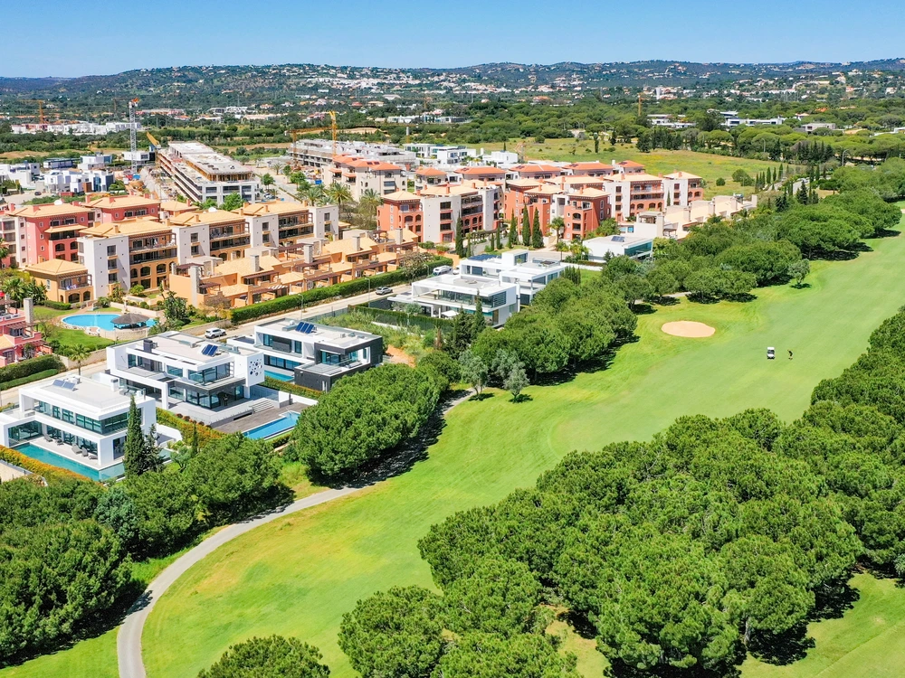 Aerial view of the lush green fairways of a golf course bordering modern luxury villas and apartments in the resort town of Vilamoura, Portugal.